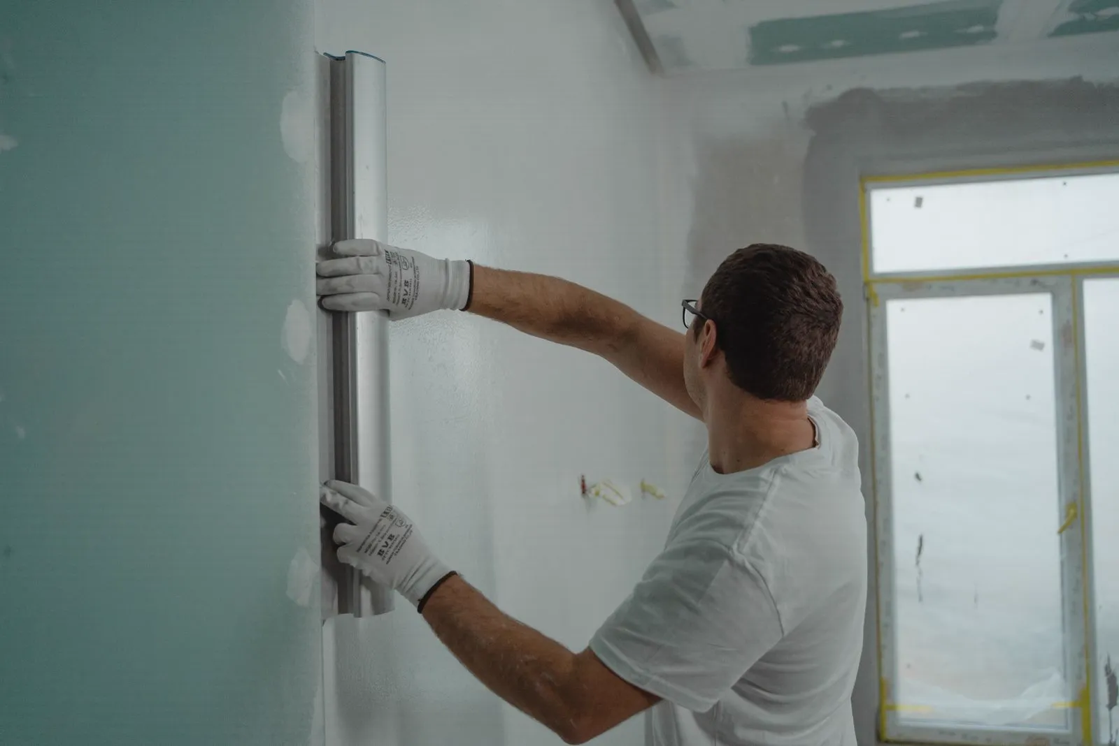 Painter in a hard hat working on a freshly prepared white wall